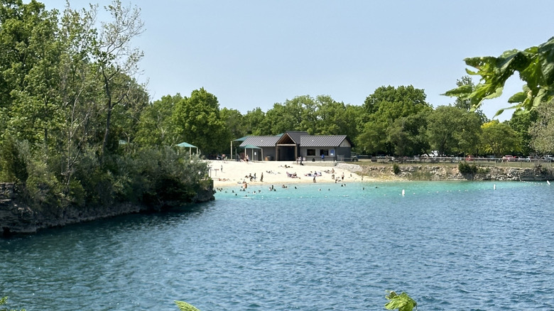 people in the distance play on the sandy beach and swim in the clear water of White Star Quarry