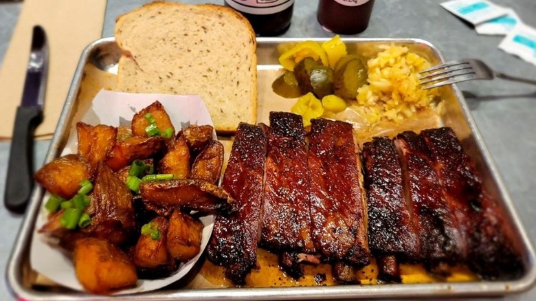 A tray of barbecue ribs with fried potatoes, pickles, and rye bread around the meat.