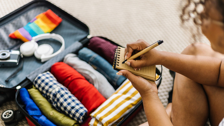 Person writing a list while in front of an open suitcase with clothing