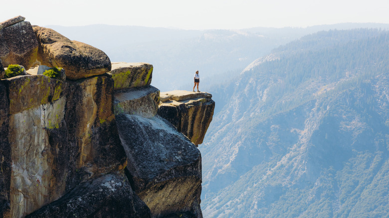 A person stands on a cliff rock outcropping in Yosemite National Park