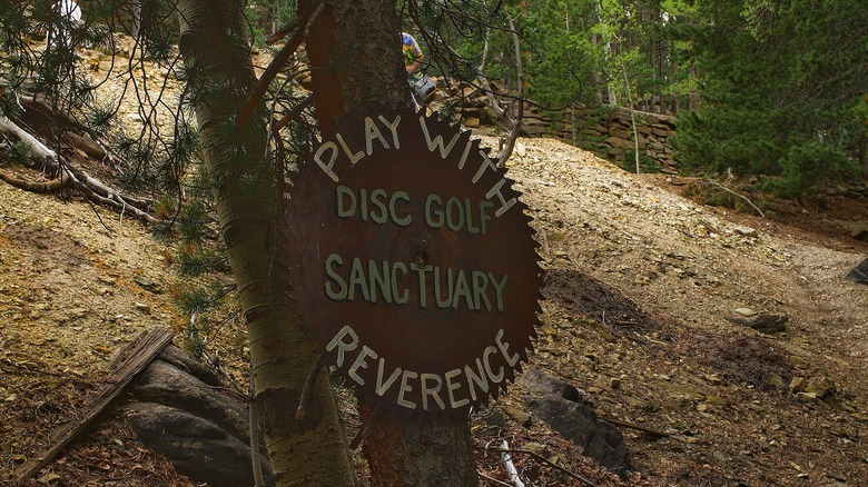 Sign in woods reading "Play with Reverence - Disc Golf Sanctuary"