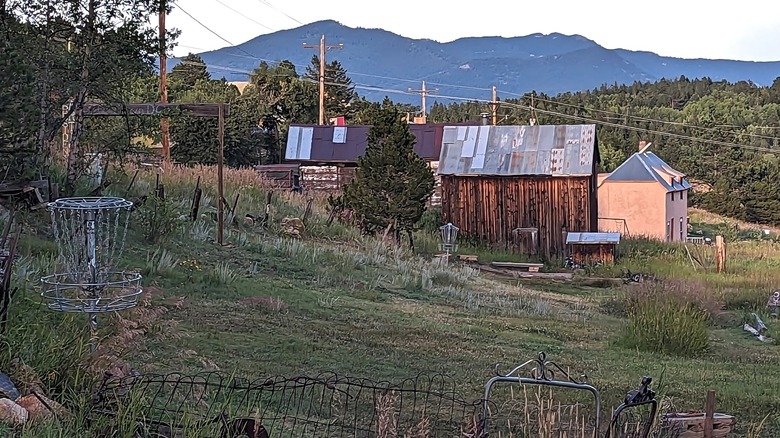 Disc golf basket in front of old buildings and mountains