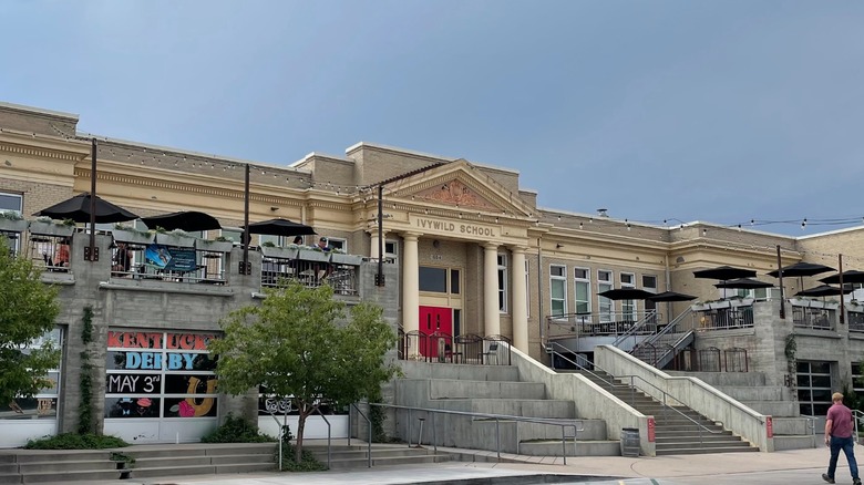 The facade of Ivywild School with patio tables and large stone stairs