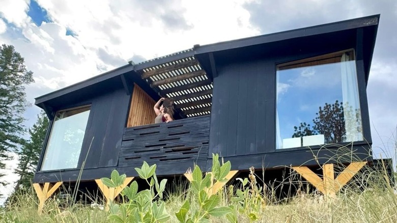 A modern black cabin with large glass windows and a wooden balcony, part of Outside Inn Nature Hotel