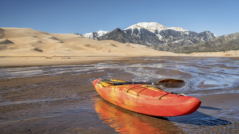 Orange kayak in the shallow waters of Medano Creek with snow-capped mountains in the background