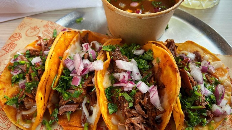 Four birria res tacos with consomé