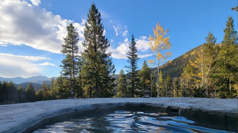 Trees and mountain range beyond a hot spring pool at Raspberry Hot Springs in Colorado