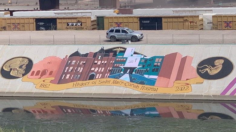 Car parked above a large mural depicting the history of Saint Mary-Corwin Hospital part of the Pueblo Levee Mural Project in Colorado