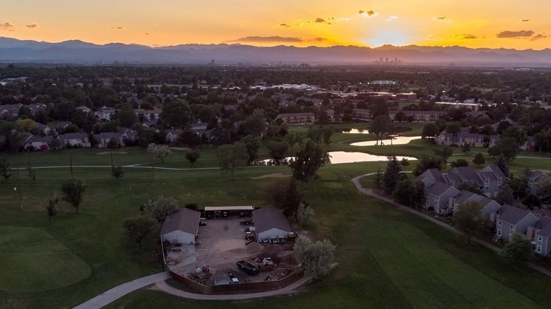 Sun sets over Rockies behind Heather Ridge golf course and neighborhood