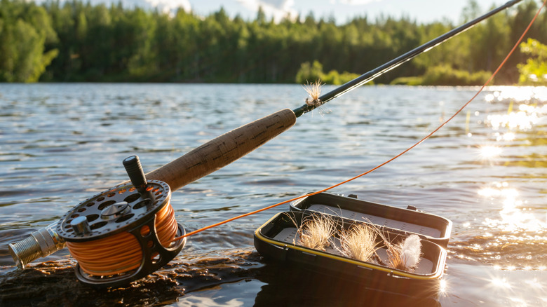 A close up of a fly rod and a box of flies on a river in the sunlight
