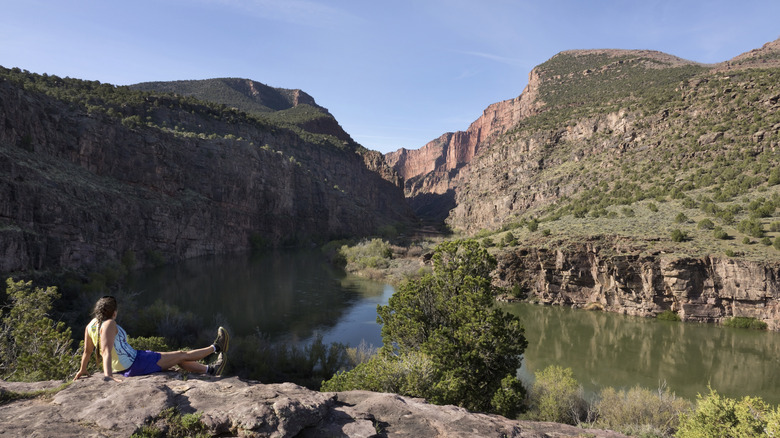 With the canyon Gates of Lodore and the Green River in the background, a woman with a ponytail relaxes on a overlook at the end of the trail in Dinosaur National Monument in Colorado