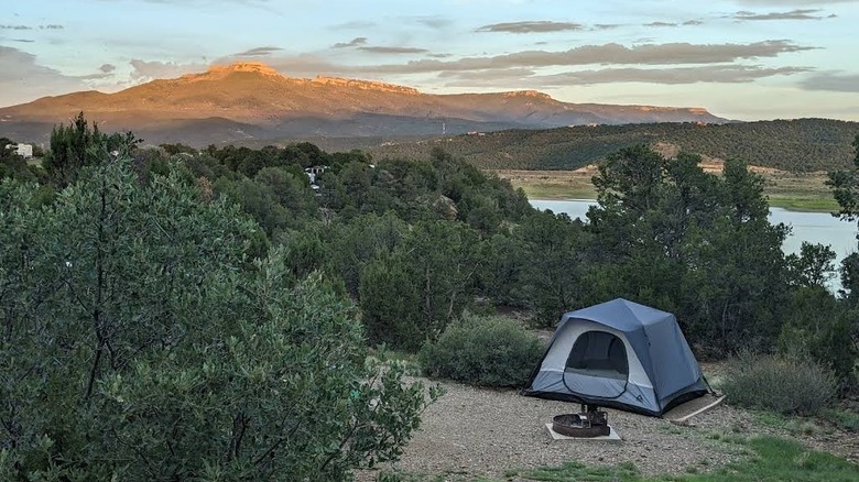 A small tent next to a fire pit surrounded by trees with a mountain in the distance at Trinidad Lake State Park in Colorado