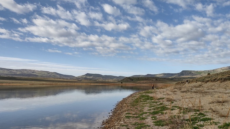 Clouds reflect on Miramonte Reservoir with man standing on shore