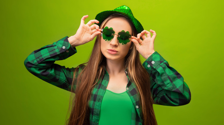 Woman wearing all green, shamrock-shaped glasses and a green party hat