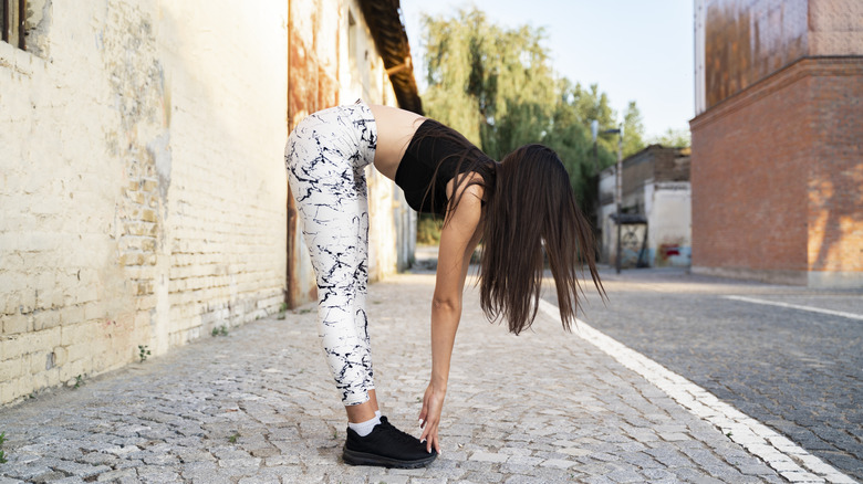 Woman side view stretching before run, in an urban zone
