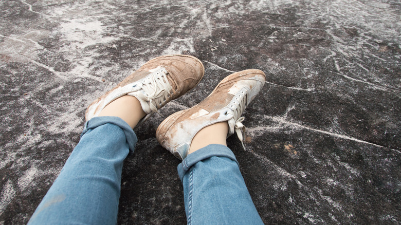 The legs of a woman wearing white sneakers. But dirty from the clay mud on stone floor background