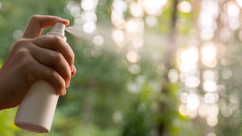 A hand spraying a bottle outdoors