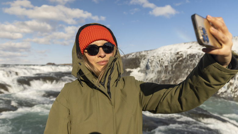 Woman taking selfie wearing sunglasses at Iceland waterfall