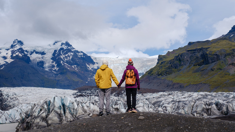 Two people standing and holding hands looking at the glacier in Iceland