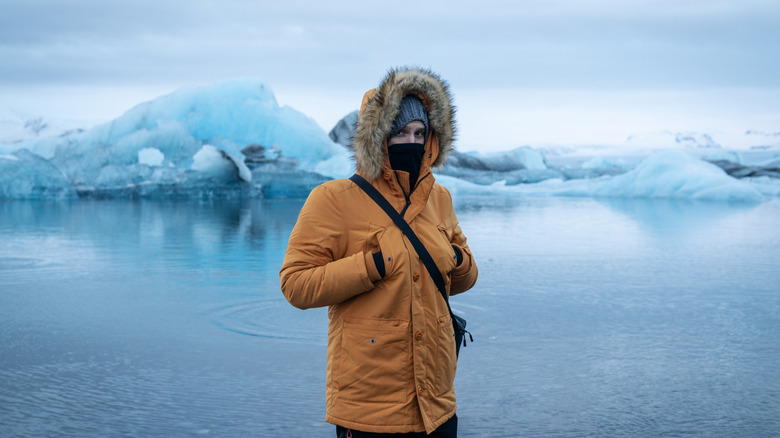 Person standing in jacket and hat in cold weather in front of icebergs in Iceland