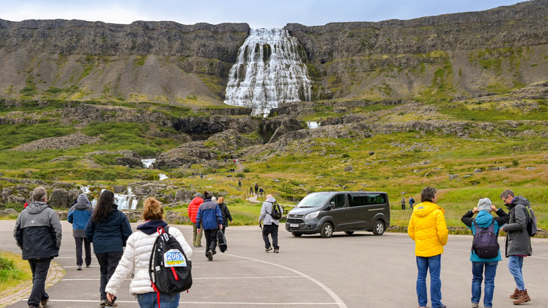 Tourists walking in a parking lot toward a waterfall in Iceland