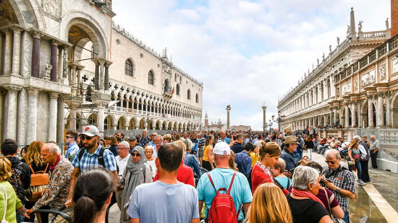 The visible effects of overtourism as cruise ship passengers crowd the walkway at the Doge's Palace in Piazza San Marco on a busy day in Venice, Italy