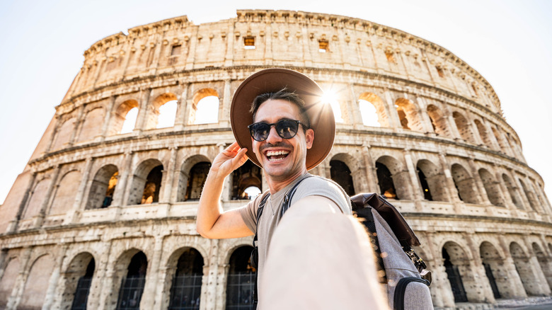 Handsome young man taking selfie with the Colosseum in the background, Rome, Italy
