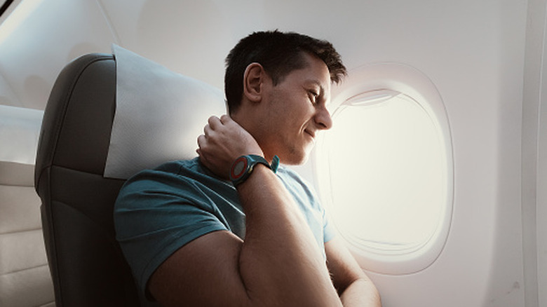 A man suffers from severe neck pain during a long flight in an uncomfortable position on an airplane