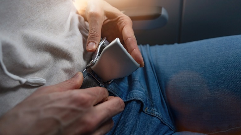 A man adjusting the seatbelt on a plane seat.