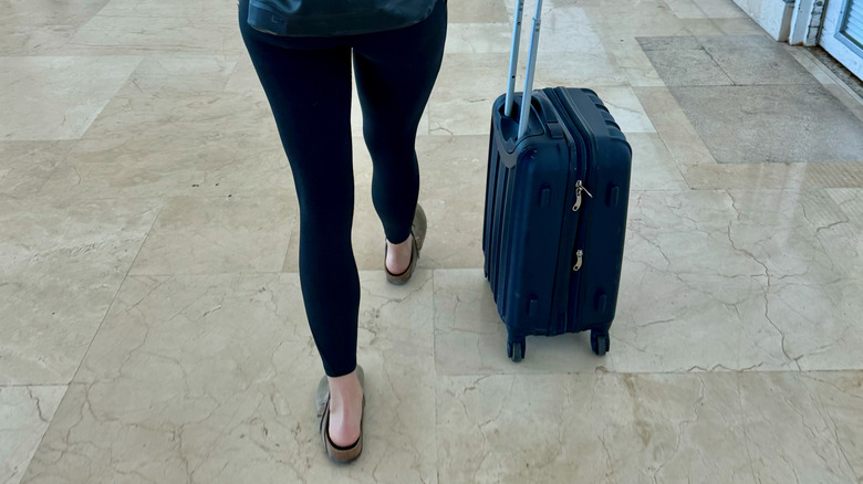 A woman pushing a suitcase wearing leggings.