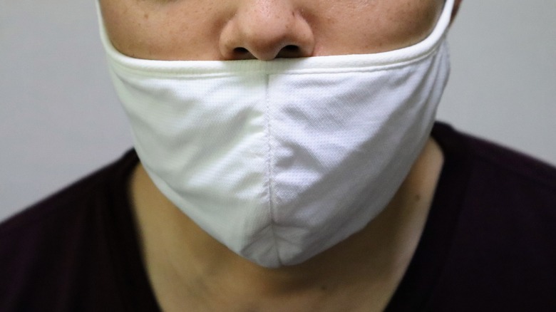 A close up of a man wering a mask incorrectly.