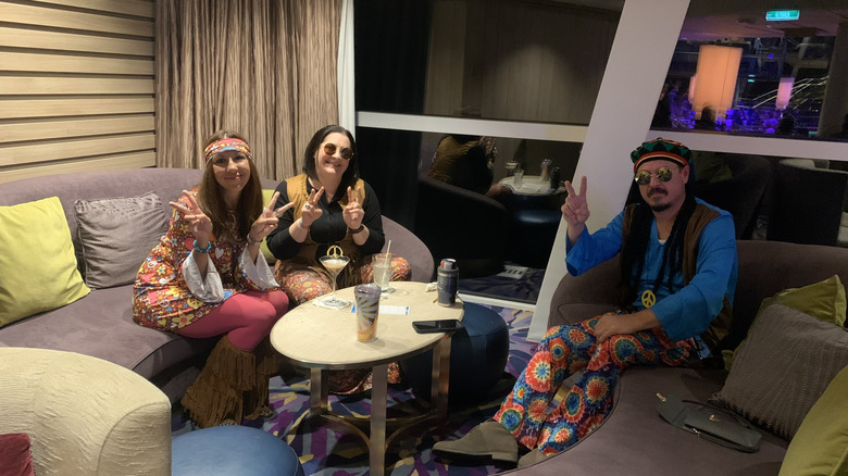Three people sitting on couches dressed in 1970s attire