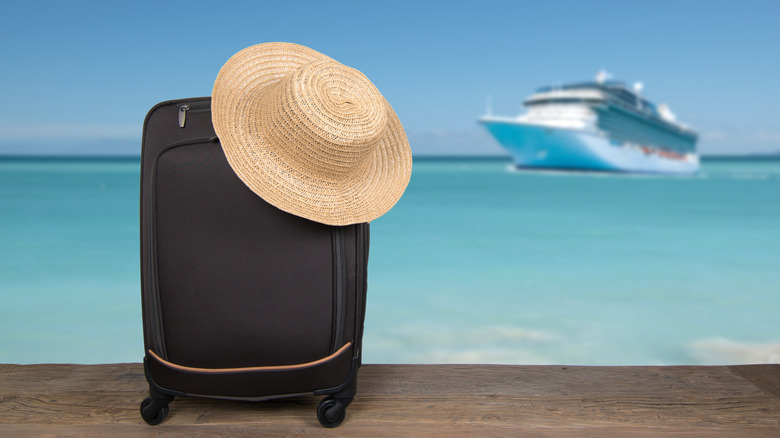 Suitcase with a straw hat on top of it, with a cruise ship in the background