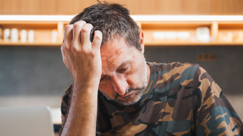 A man wearing a camouflage shirt, holding his head in his hand