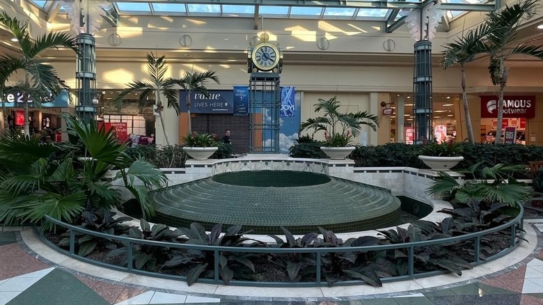 Dead fountain surrounded by plants and a clock tower with a skylight inside Concord Mall Delaware
