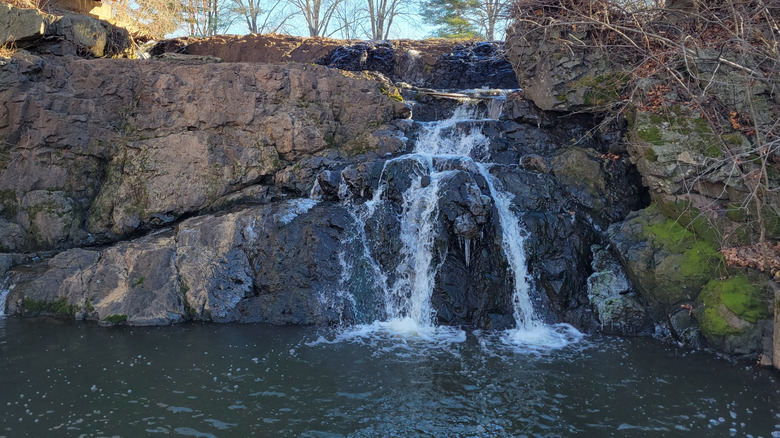 A small waterfall flows over rocks into a pond