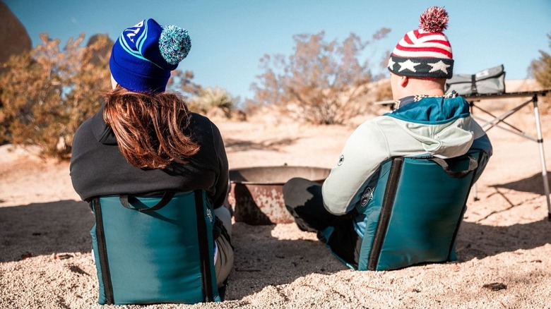 Two people using camping chairs near a firepit
