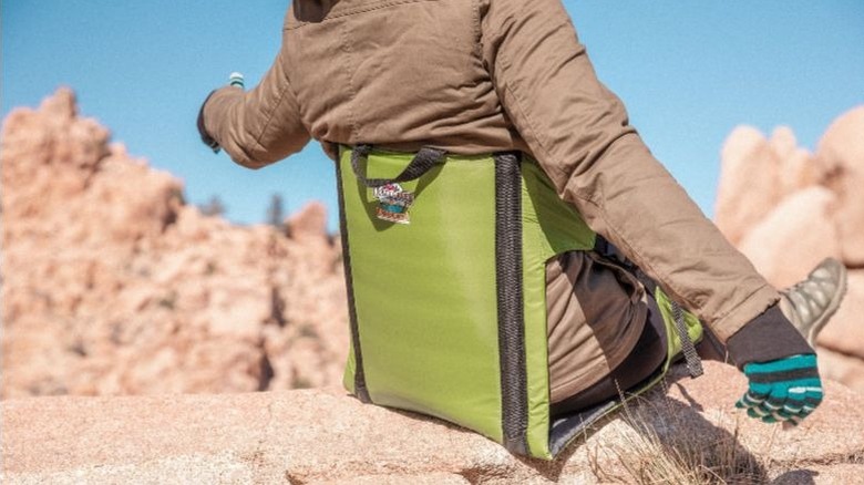 A hiker reclines in a lime green camping chair on a rocky surface.