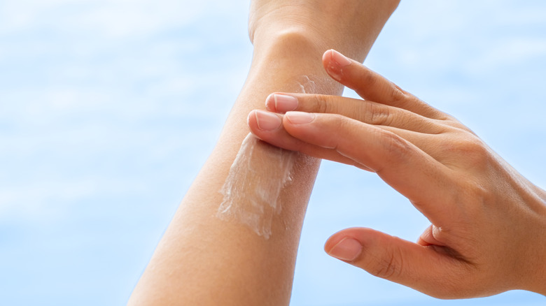 A woman's hand applying sunscreen onto her arm with two fingers.