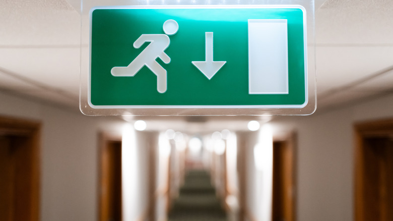 A green emergency exit sign hangs in a long hotel hallway.