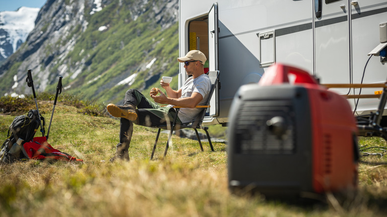 A man sipping coffee while sitting at his campsite with a power generator in the foreground