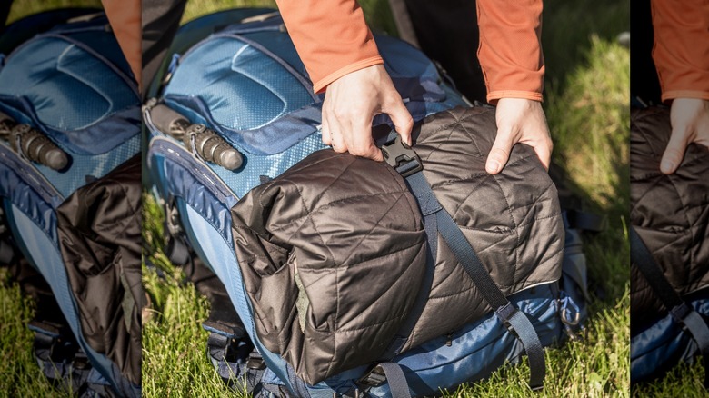 A person unhooking a strap on the back of a backpack with a sleeping bag