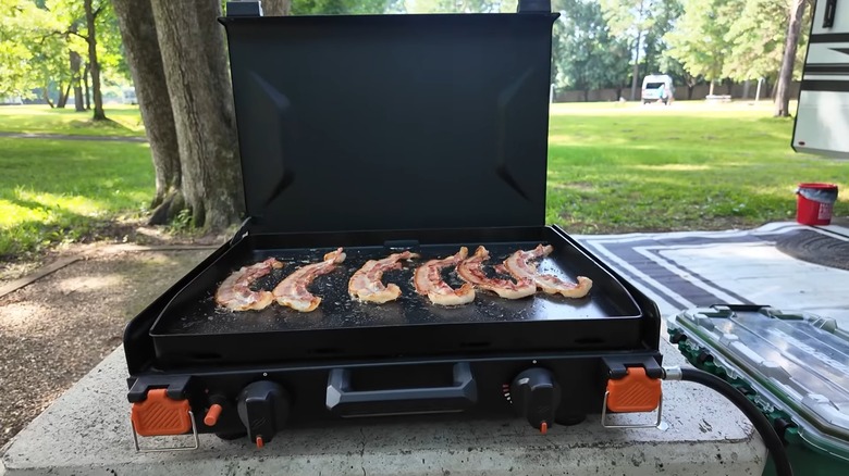 A Blackstone griddle on an outdoor table with trees and an RV in the background