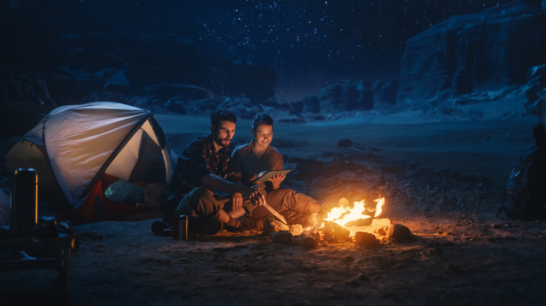 A couple camping in a canyon at night sits around a campfire.