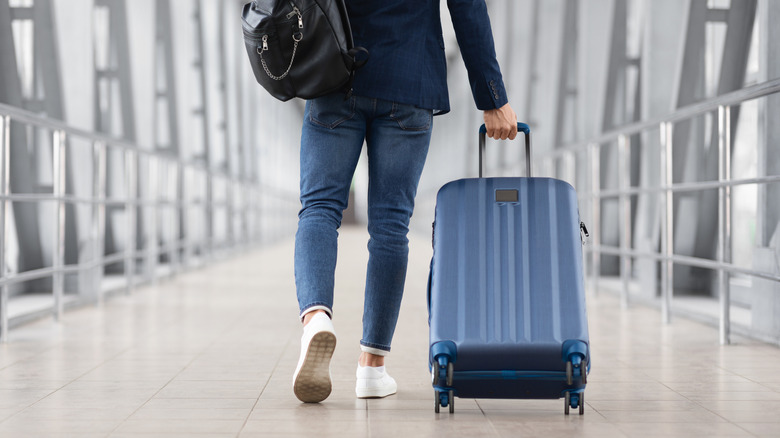 Man walking ahead while rolling a suitcase
