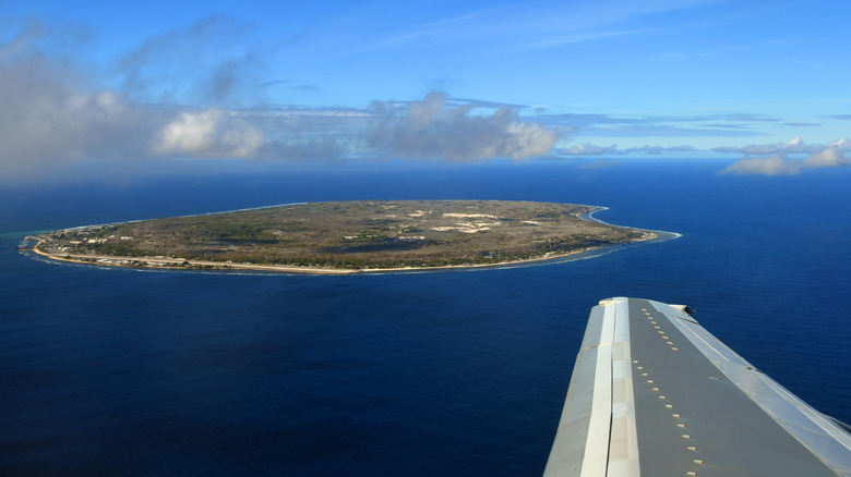 Tiny island surrounded by Pacific ocean as seen from plane wing