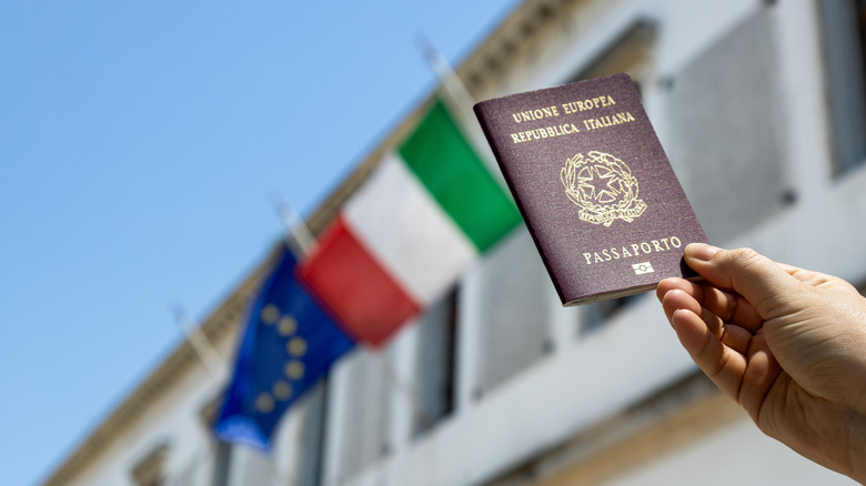 Italian passport held up to building with the Italian and EU flags