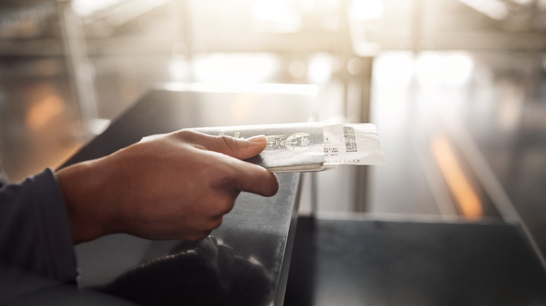 Person's hand giving over passport and boarding pass