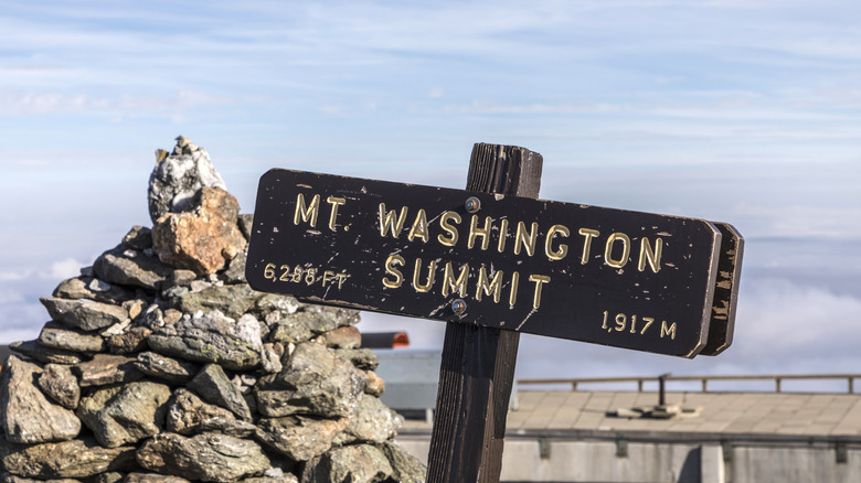 Mount Washington Summit sign with rock cairn and blue sky behind it