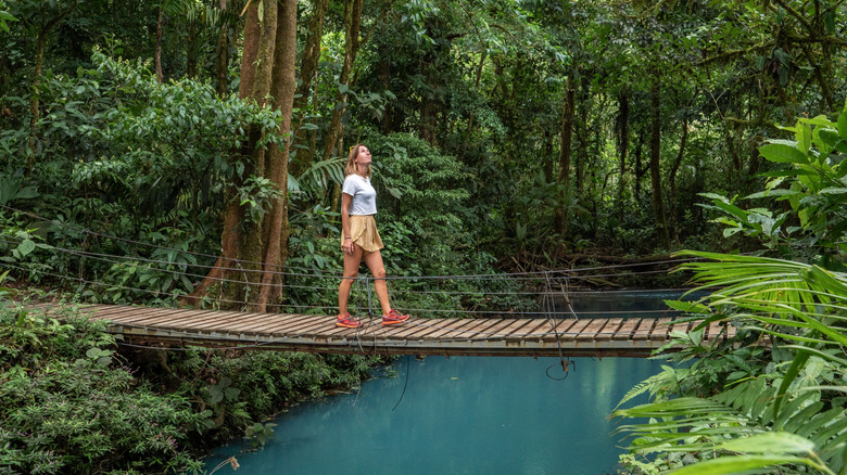 Woman crossing a bridge in the jungle over the turquoise Rio Celeste river in Costa Rica